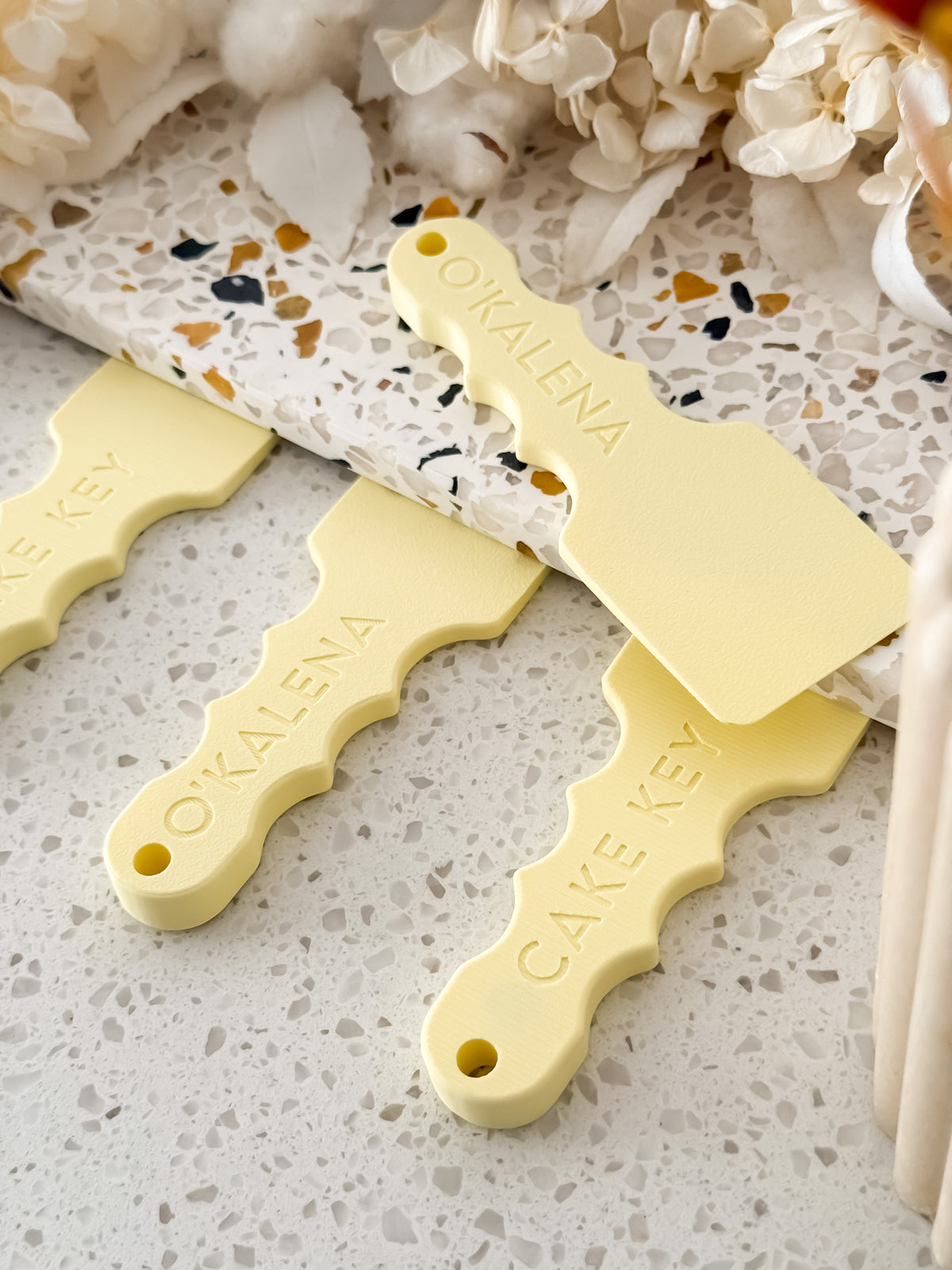 Cake Key™ cake board lifting tools with embossed lettering and keyring holes on a terrazzo bench