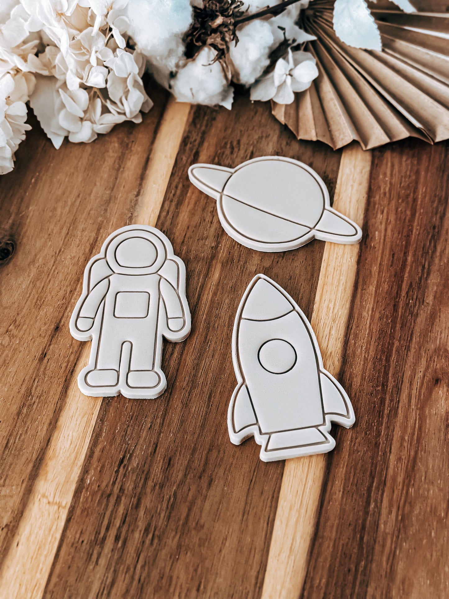 Wooden cutouts of an astronaut, planet, and rocket on a wooden surface with cotton and paper decorations.