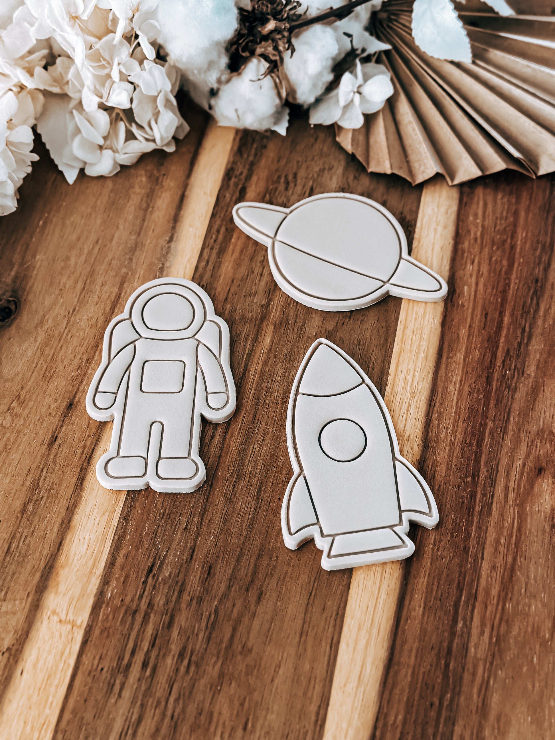 Wooden cutouts of an astronaut, planet, and rocket on a wooden surface with cotton and paper decorations.